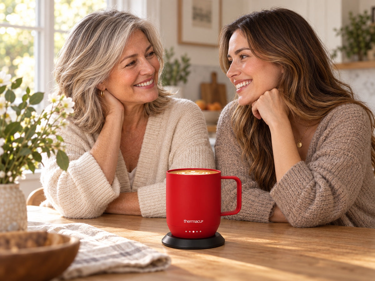 A mother in her sixties sharing a quiet coffee moment with her adult daughter and a red Thermacup